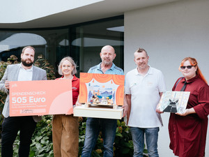 Teilnehmende und Mitarbeitende aus dem Beruflichen Trainingszentrum Cottbus übergeben einen Scheck und ein Puppentheater an das Team des Johanniter-Kinderhauses "Pusteblume"