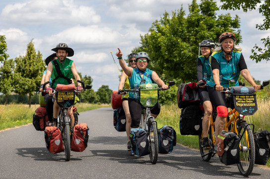 Radler und Radlerinnen fahren als Tandems auf der Mut-Tour der Mut-Tour über eine Straße.