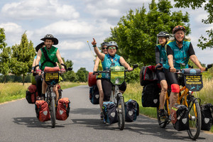 Radler und Radlerinnen fahren als Tandems auf der Mut-Tour der Mut-Tour über eine Straße.